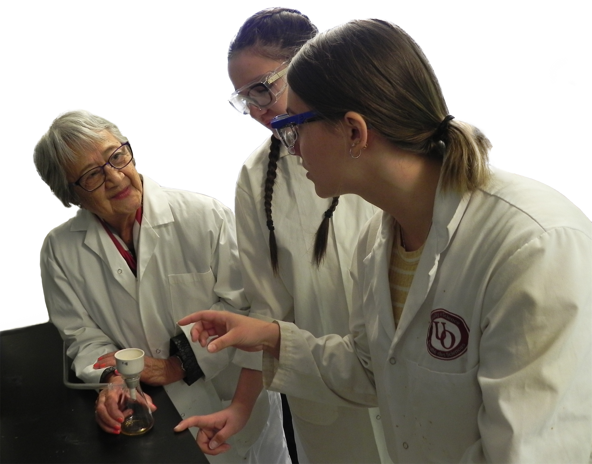 Picture of Verna J. Kirkness and two students talking in a lab. Everyone is wearing a lab coat and googles.